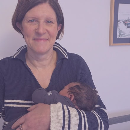 Maria the Doula smiling whilst soothing and cuddling a newborn during a postnatal doula session
